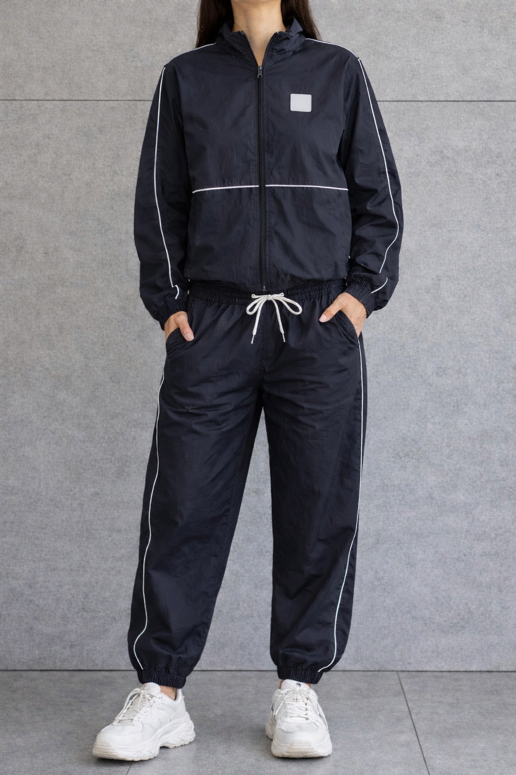 Person wearing a black windbreaker tracksuit with white accents against a gray background